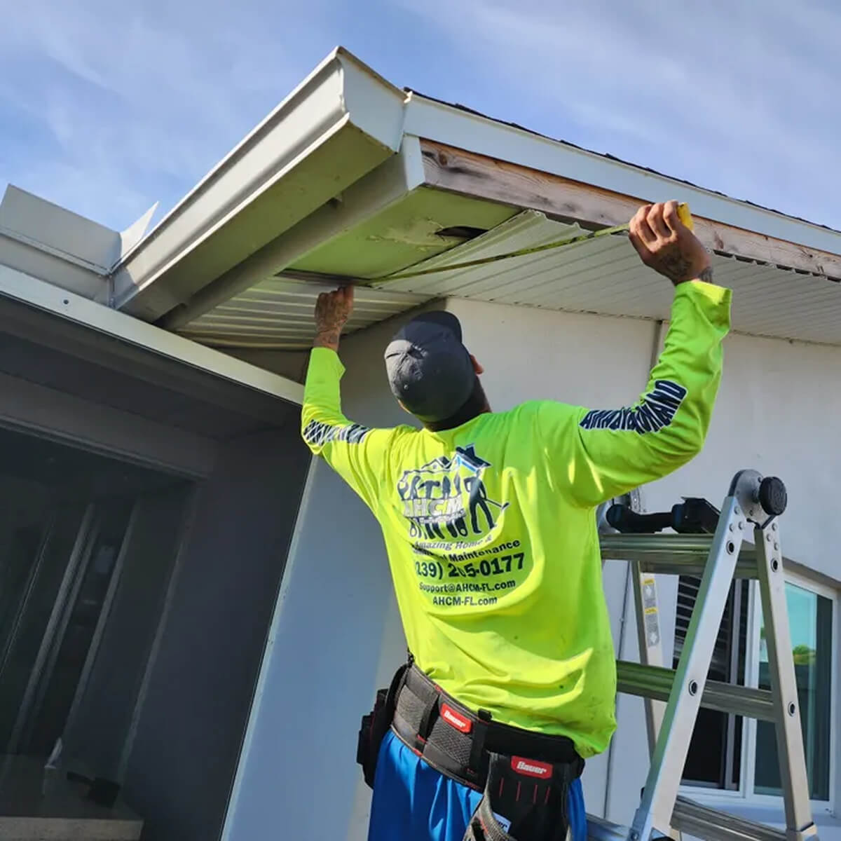 Worker inspecting roof soffit on ladder.