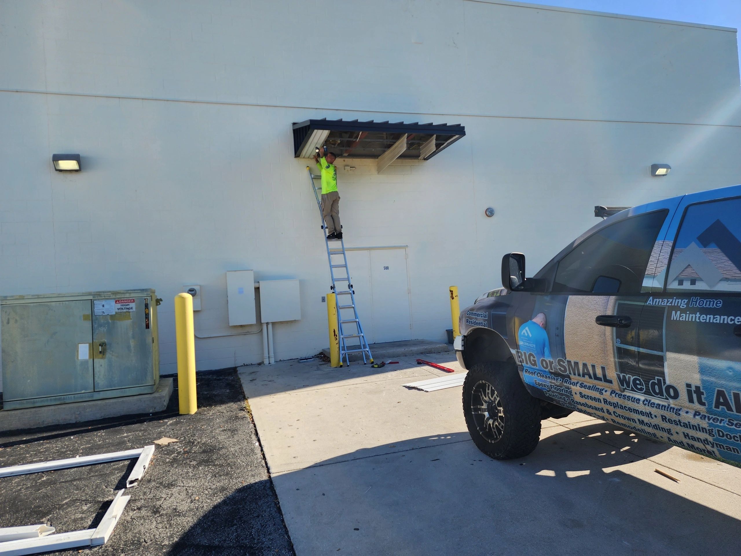 Worker on ladder repairing awning near service truck