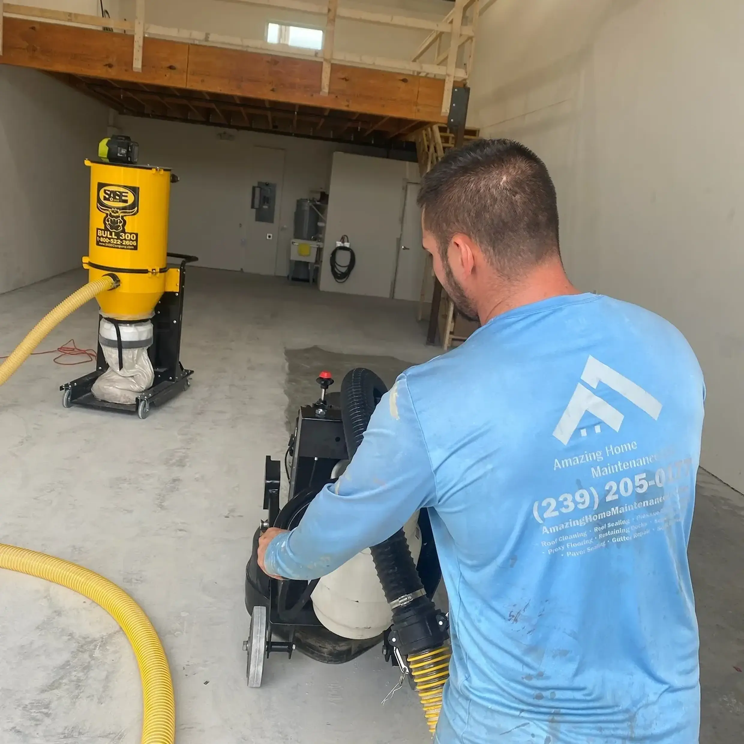 Worker operating concrete floor grinder with vacuum