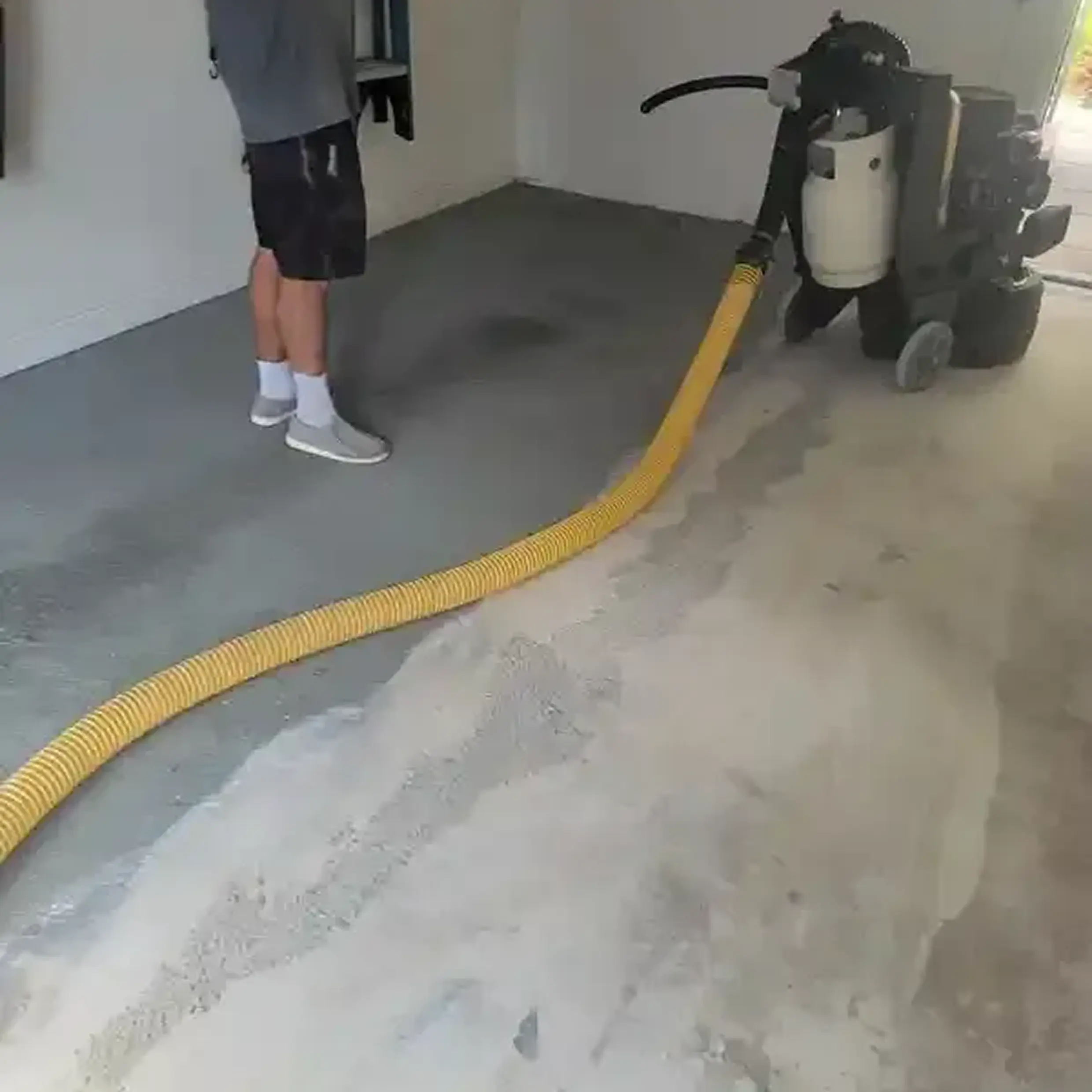 Person operating concrete grinder with yellow hose