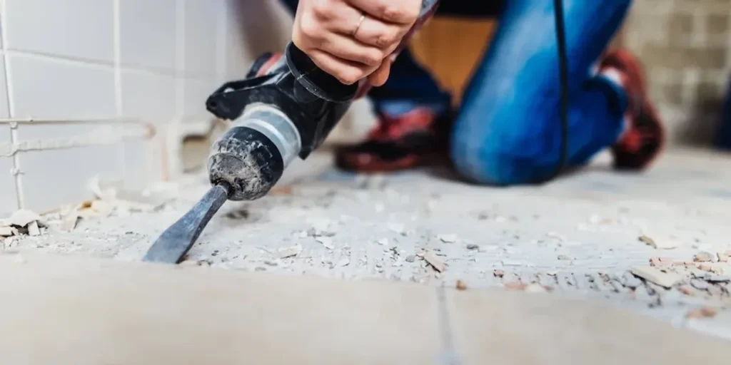 Worker using demolition hammer to remove tiles