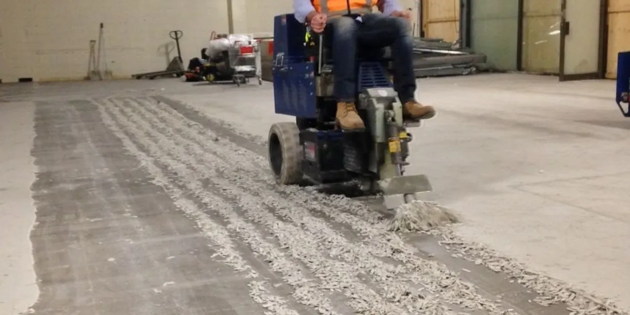 Worker operating floor grinder removing concrete surface