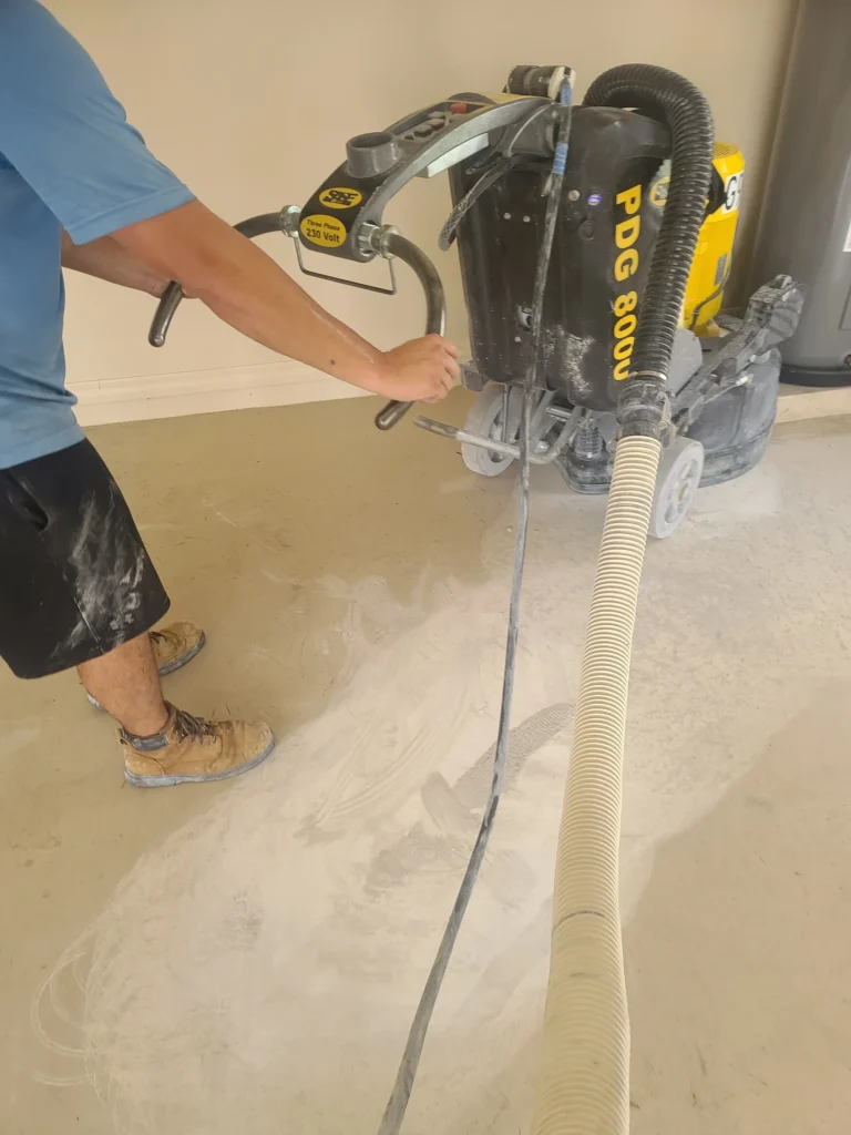 worker operating concrete floor grinder with vacuum