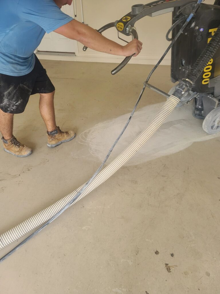 Worker operating concrete floor grinder and vacuum