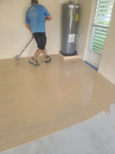 Worker applying epoxy floor coating near water heater