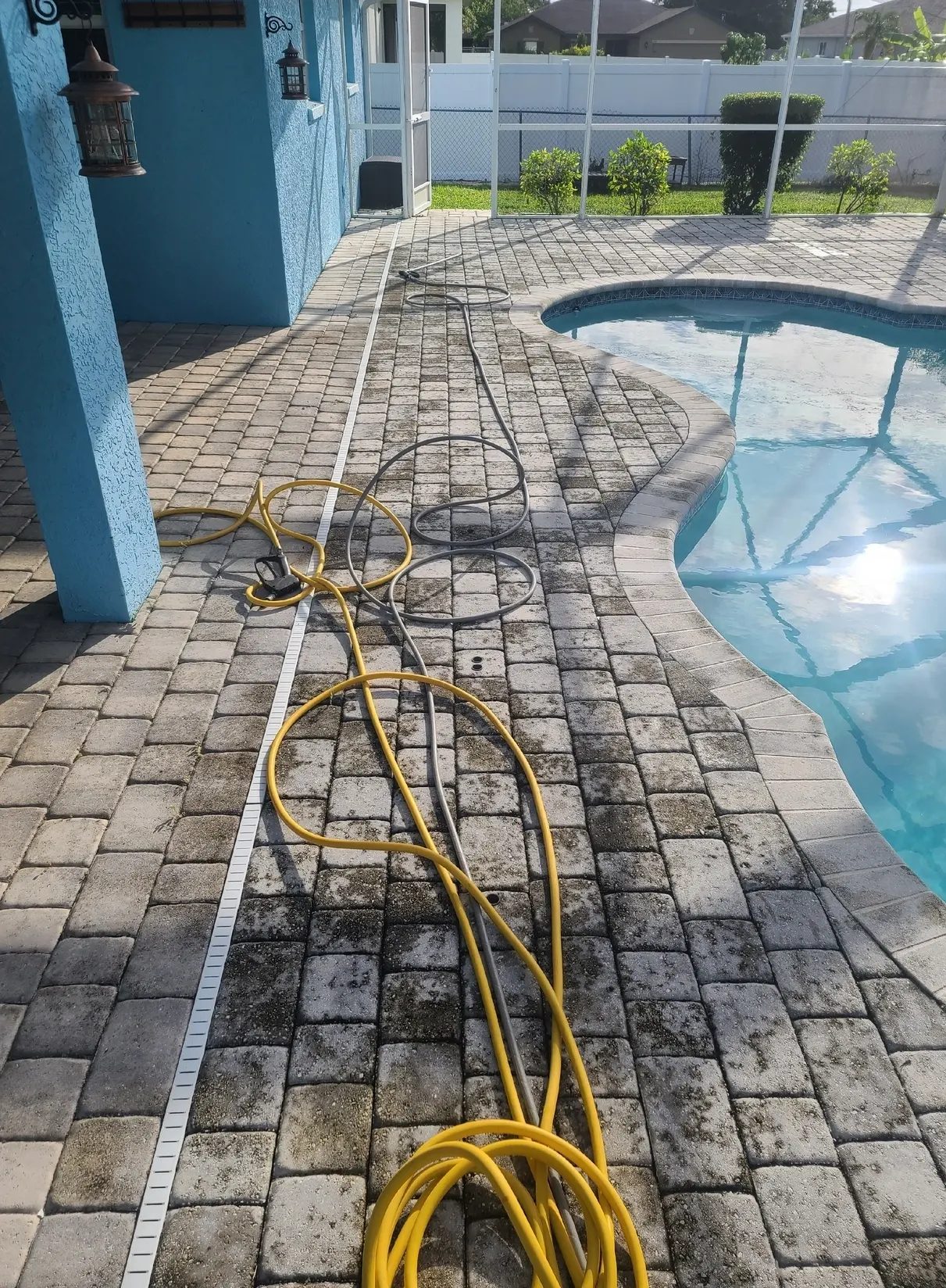 Coiled yellow hose on poolside paver deck