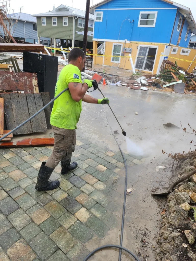 Worker pressure-washing flooded driveway near houses