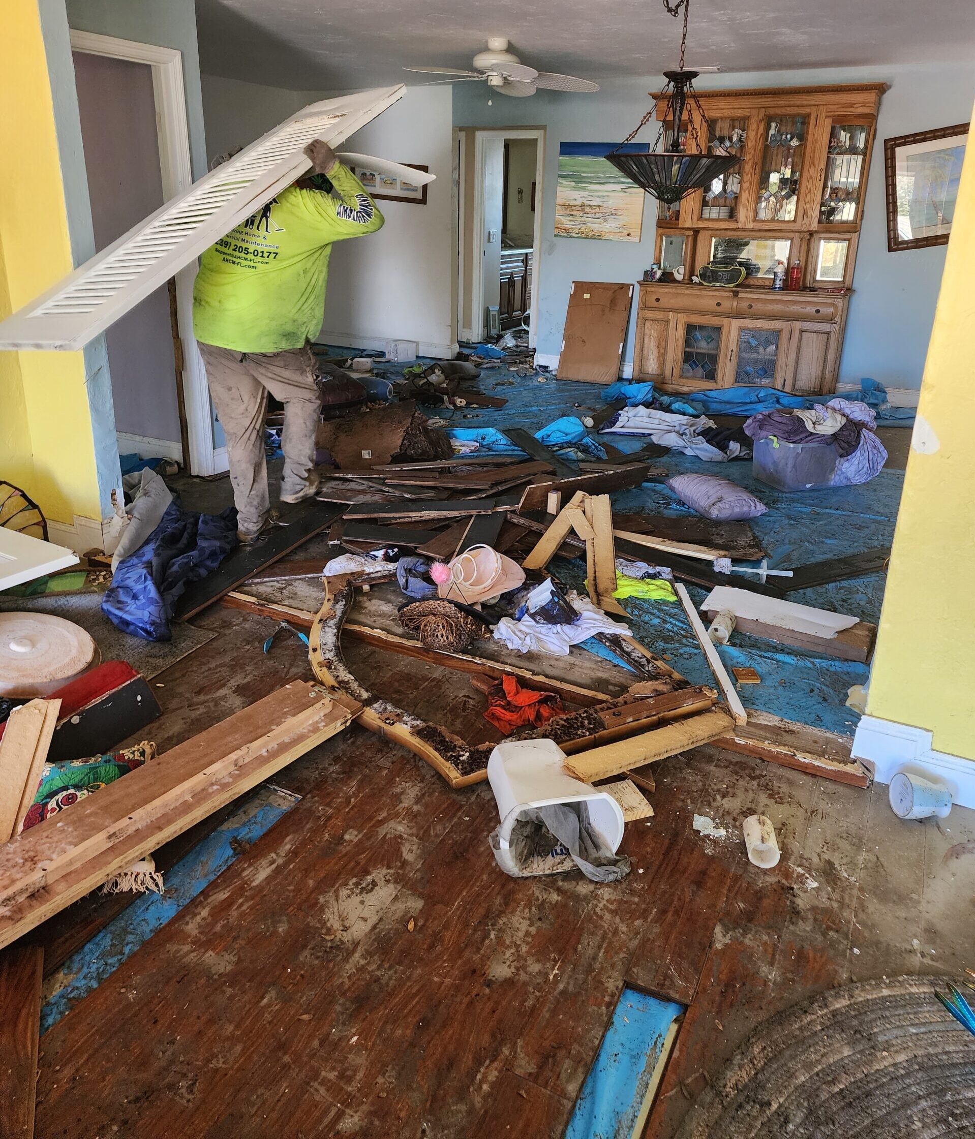 Worker clearing debris in flood-damaged living room