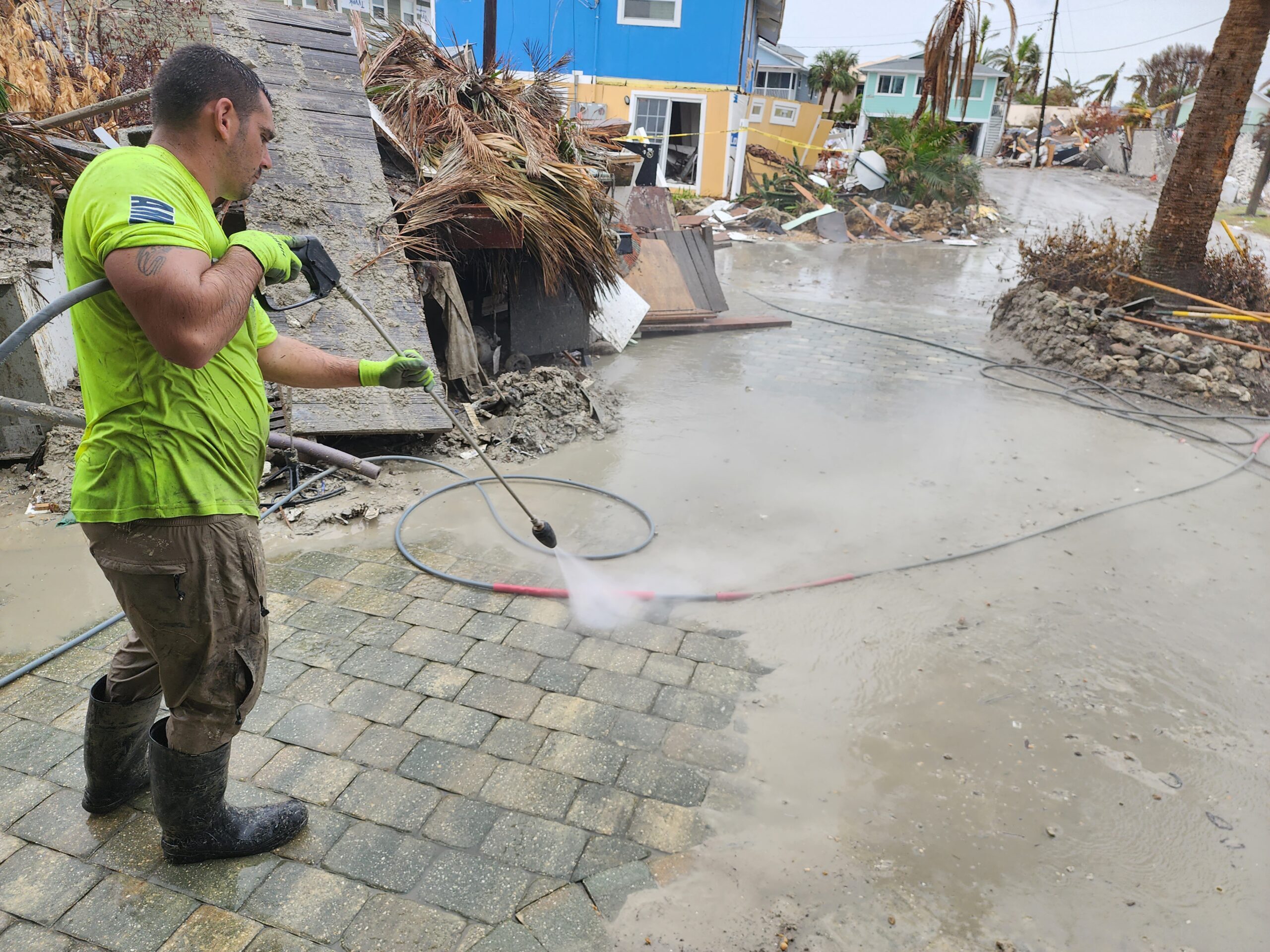 Worker pressure-washing flood debris on street