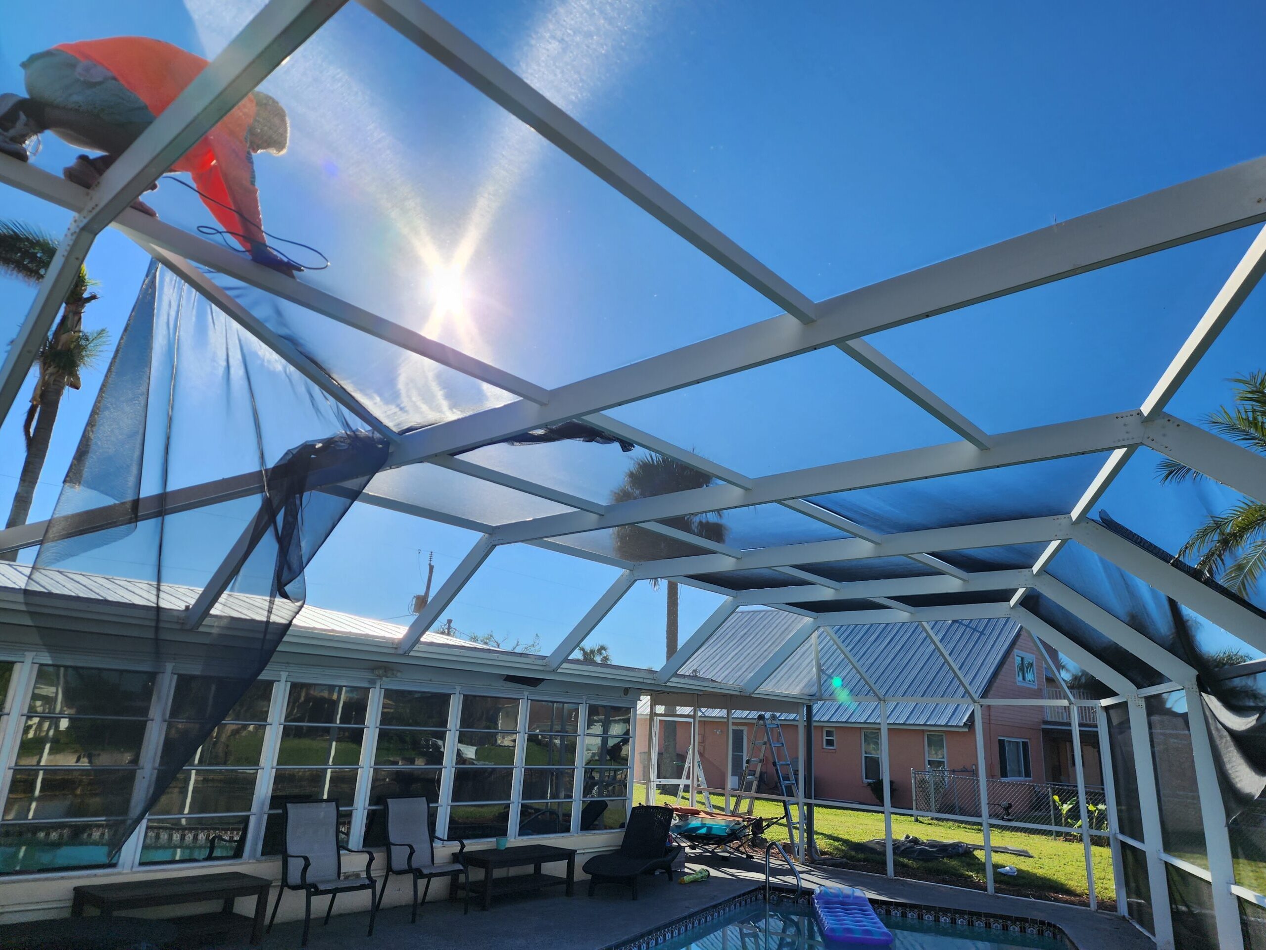 Worker fixing screened pool enclosure under sun