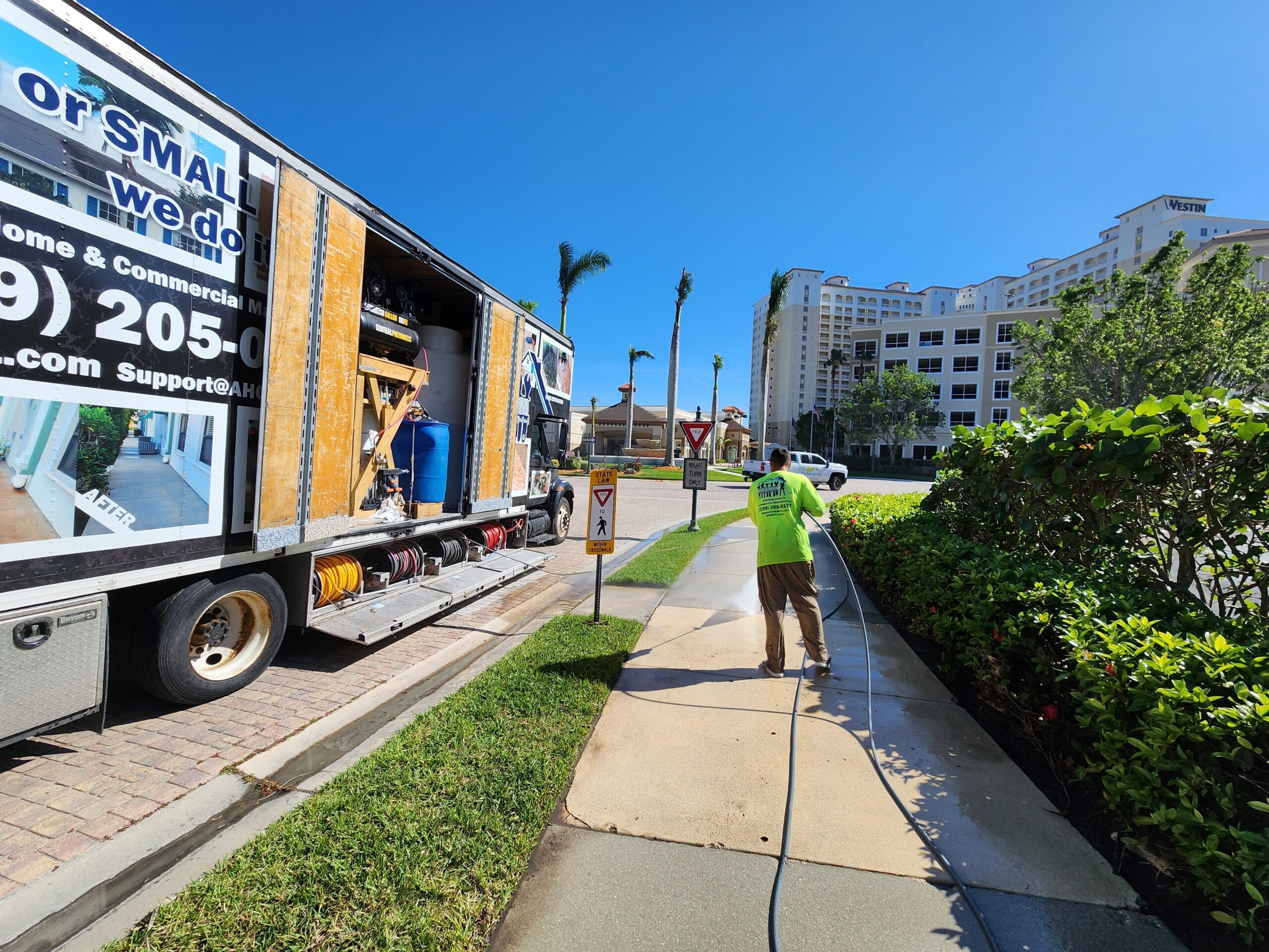 Worker pressure-washing sidewalk near service truck
