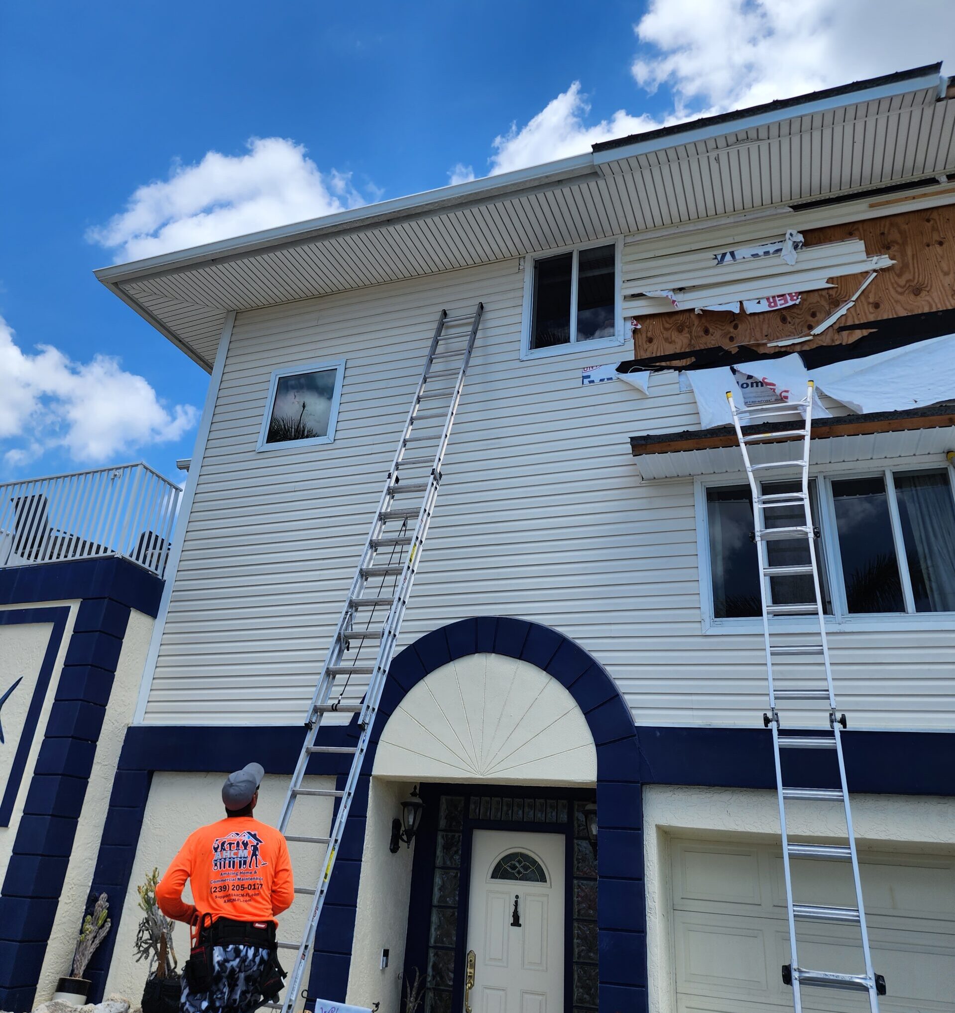 Worker inspecting damaged house siding with ladders