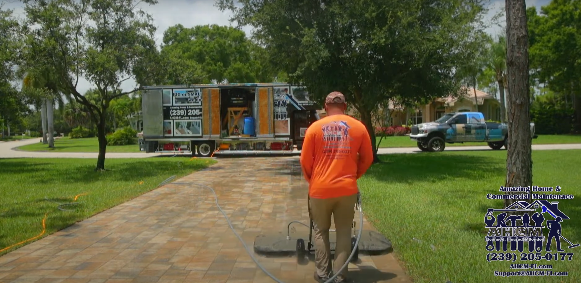 Worker pressure-washing paver driveway near trucks