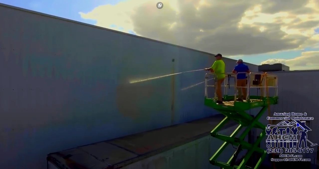 Two workers pressure-washing a large exterior wall