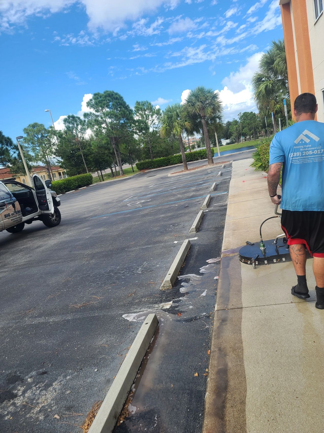 Worker pressure-washing sidewalk by parking lot