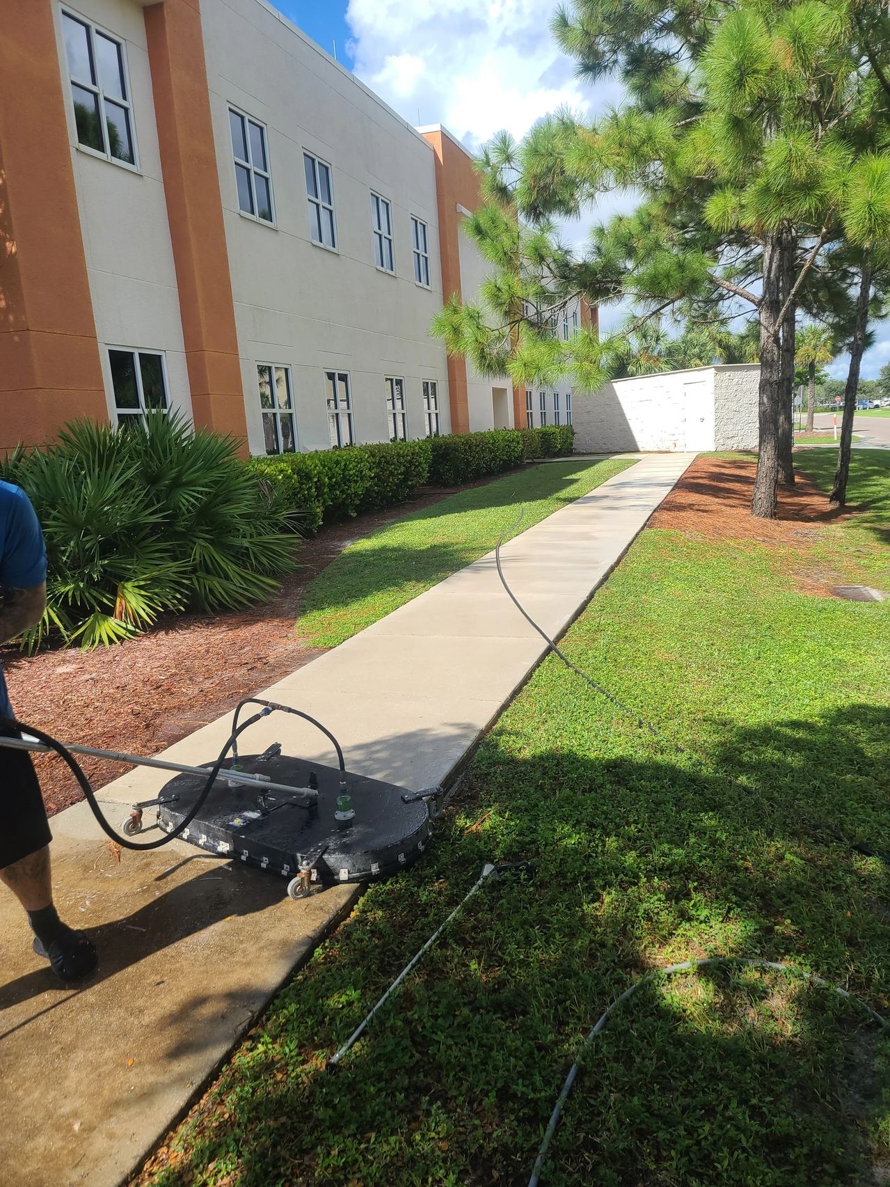 Worker pressure-washing sidewalk outside building