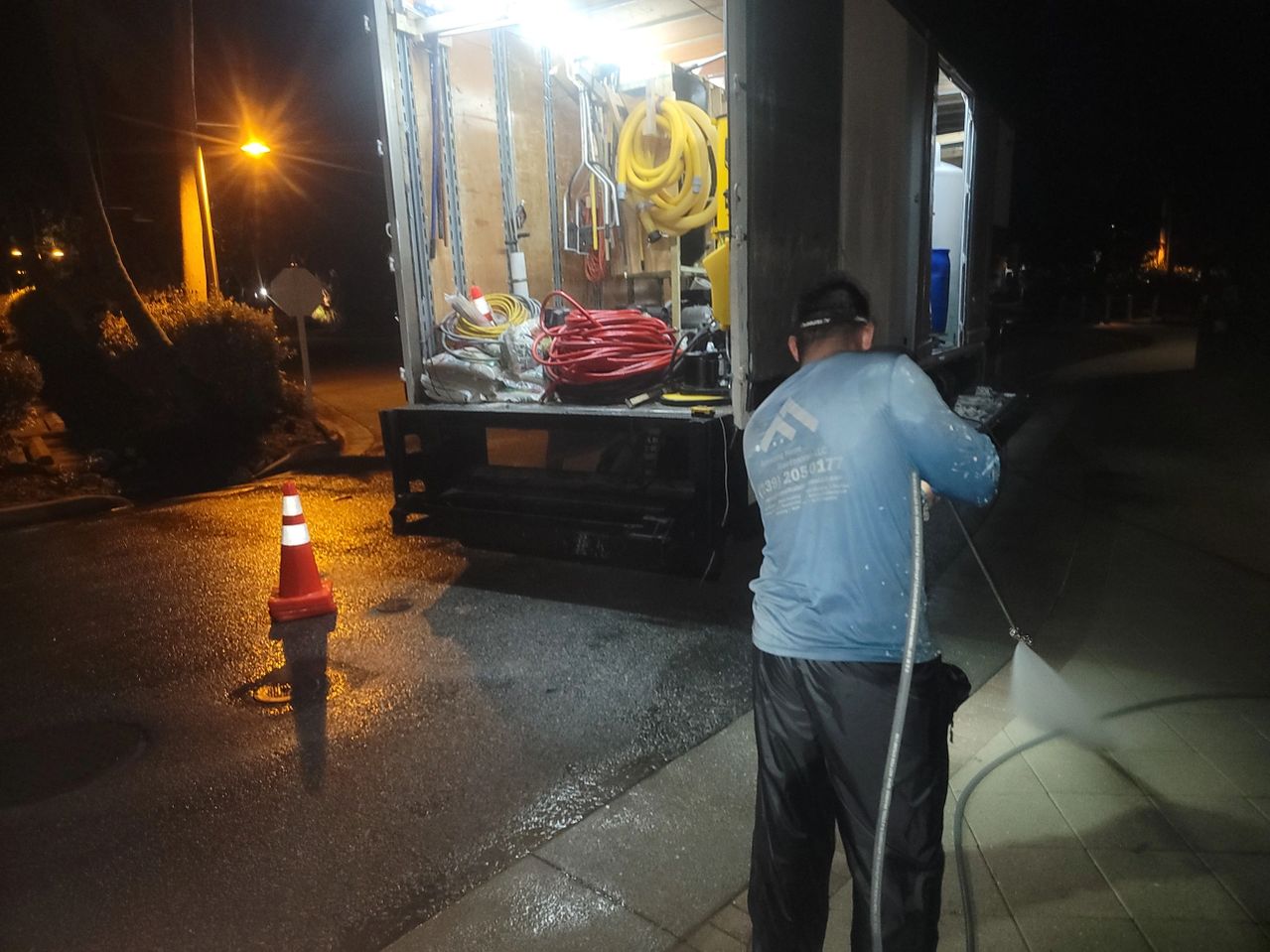 Worker pressure-washing sidewalk near utility truck