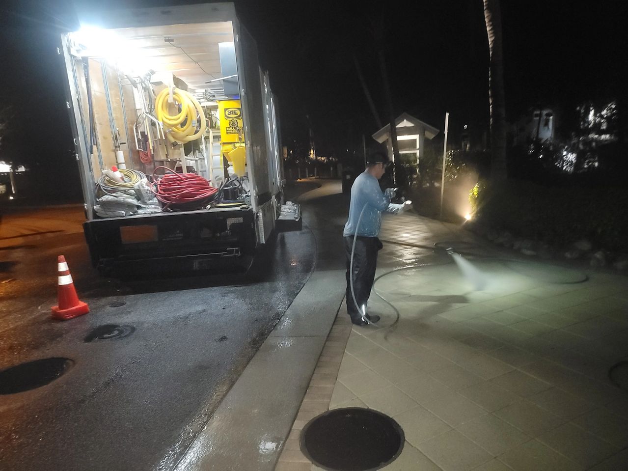 Worker pressure-washing sidewalk at night