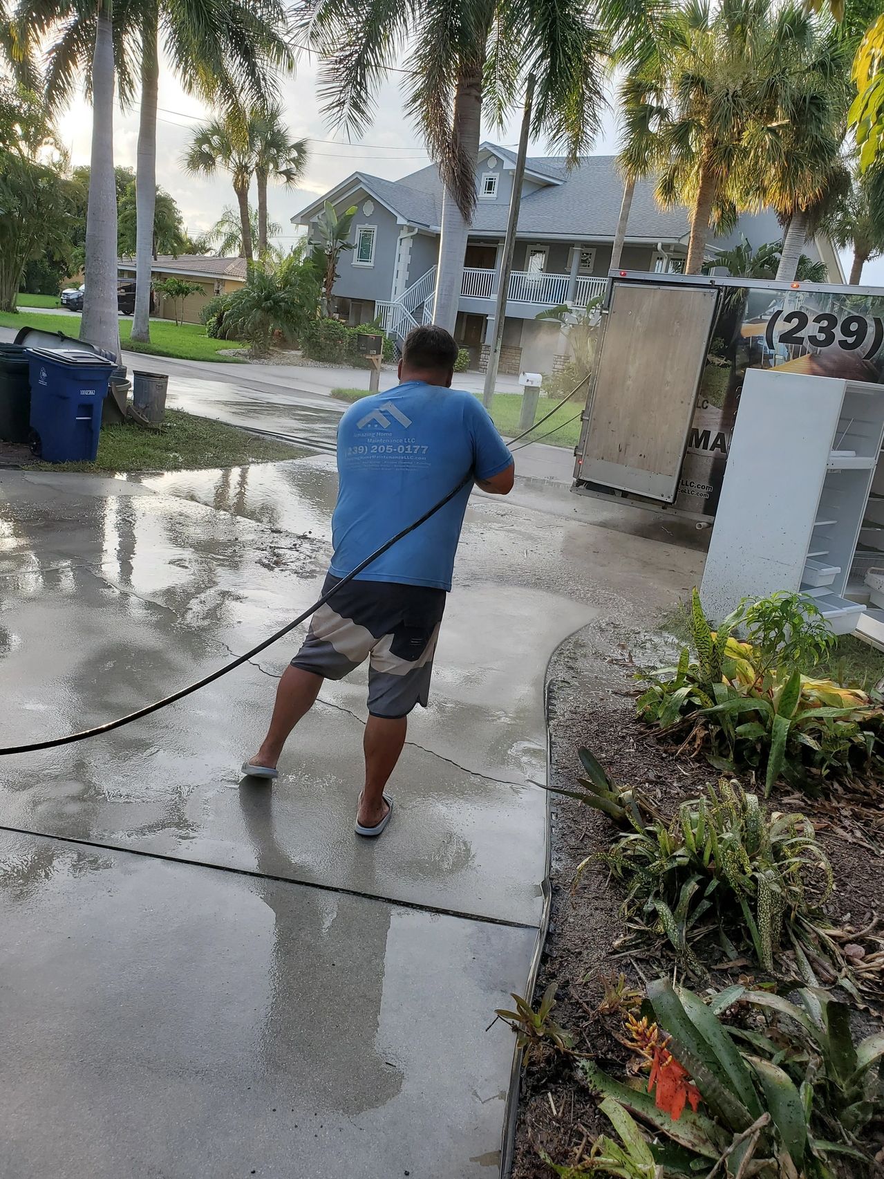 Worker pressure-washing residential driveway amid palm trees