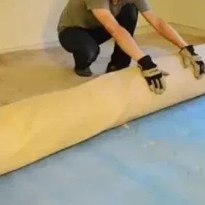 Person rolling up beige carpet in room