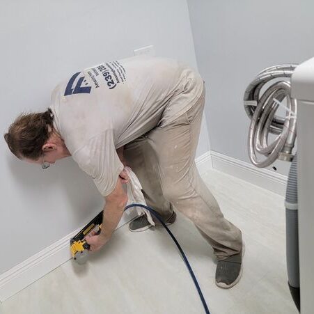 Worker installing baseboard trim with pneumatic nailer