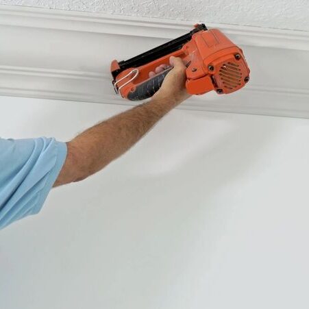 Worker installing crown molding with nail gun