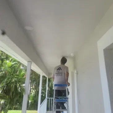 Worker on ladder painting exterior porch ceiling