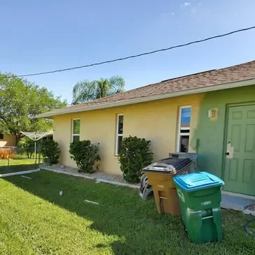 Yellow house with green door and trash bins