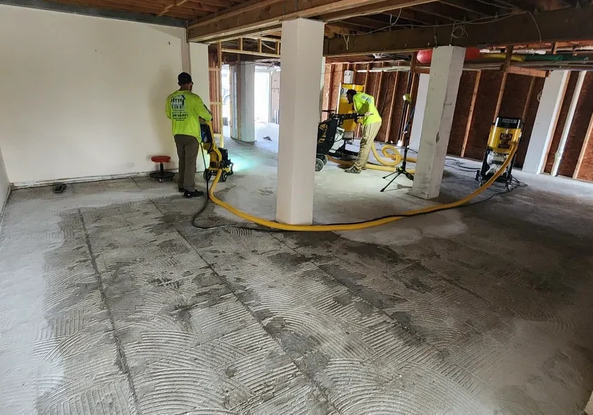 Workers grinding concrete floor in basement renovation