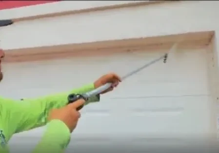 Worker sealing garage door frame with caulking gun