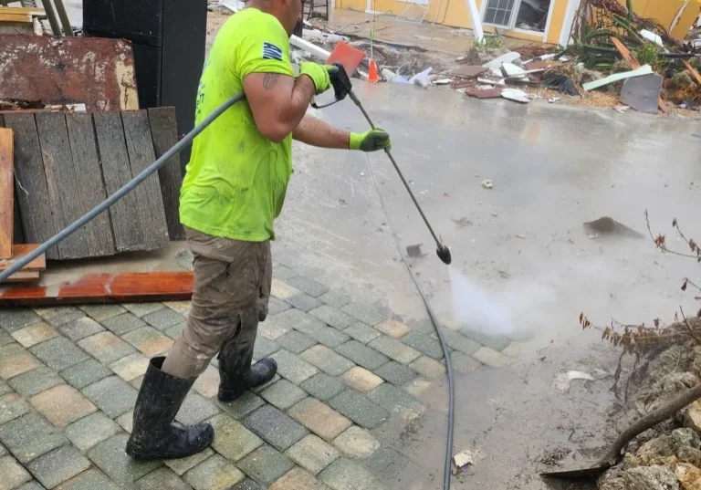 Worker pressure-washing flooded driveway near houses