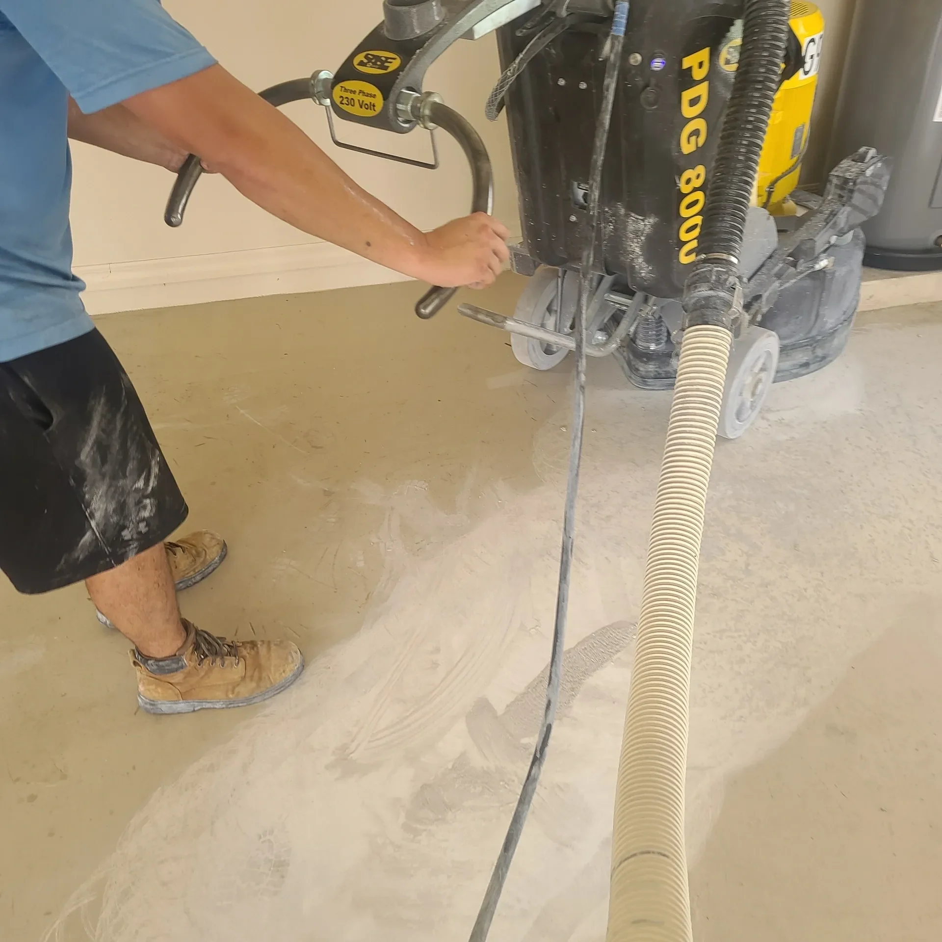 worker operating concrete floor grinder with vacuum