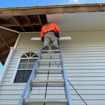 Worker on ladder repairing house soffit