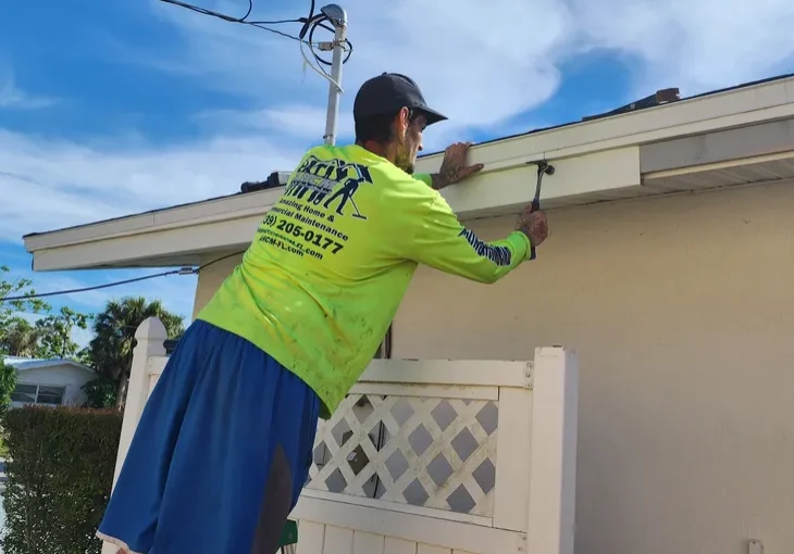 Worker cleaning gutter on ladder at house